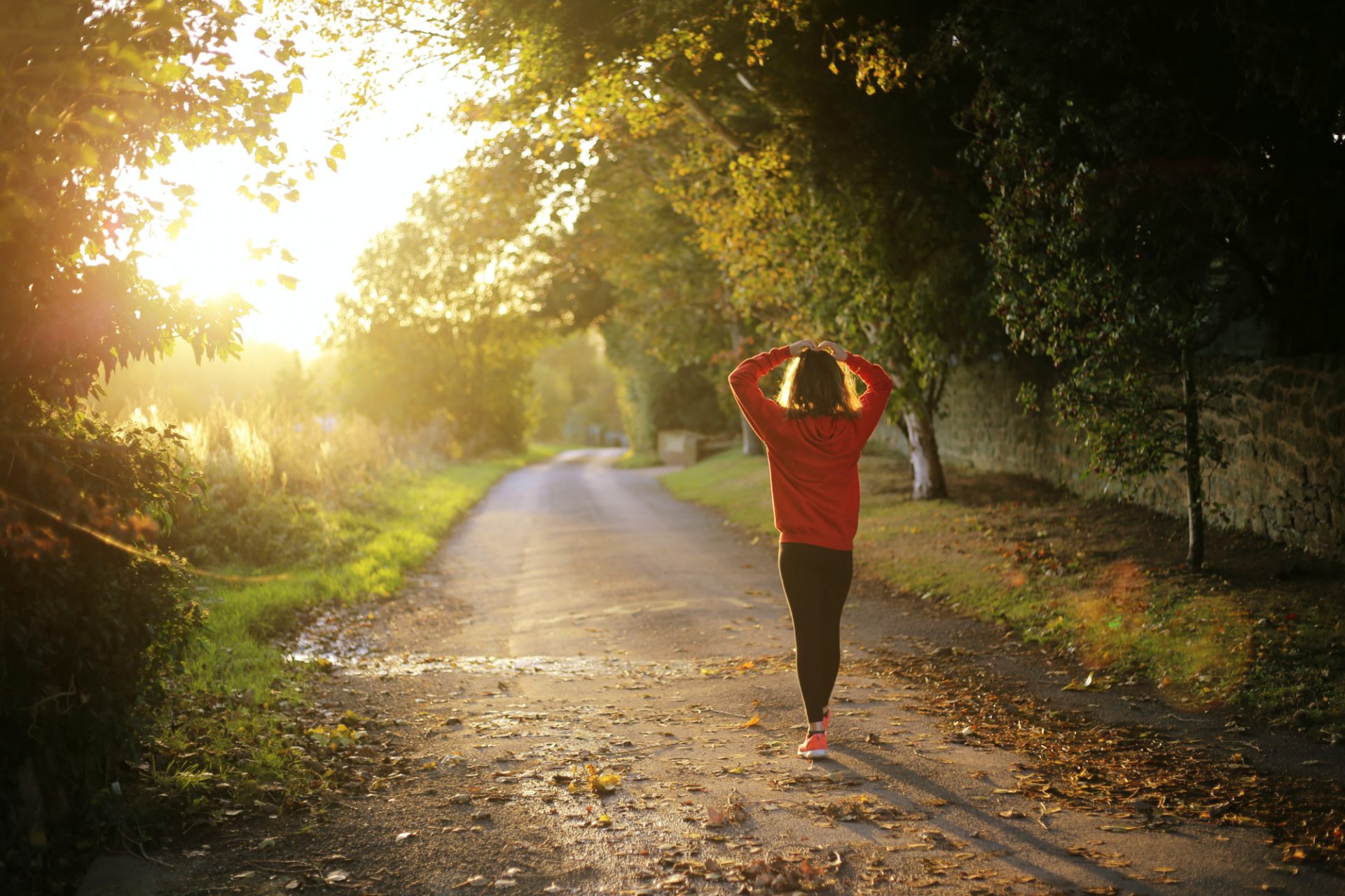 A woman in a red sweatshirt strolls through a sunny park